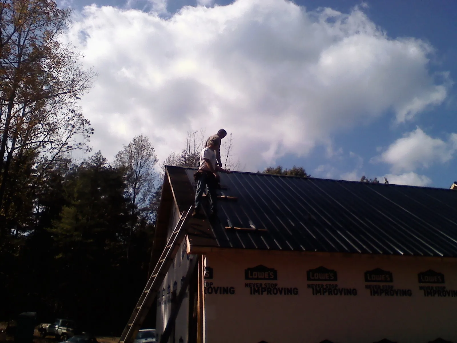 Roofer fastening dark metal panels high against a cloudy sky, from a Roof Inspection job in Litchfield