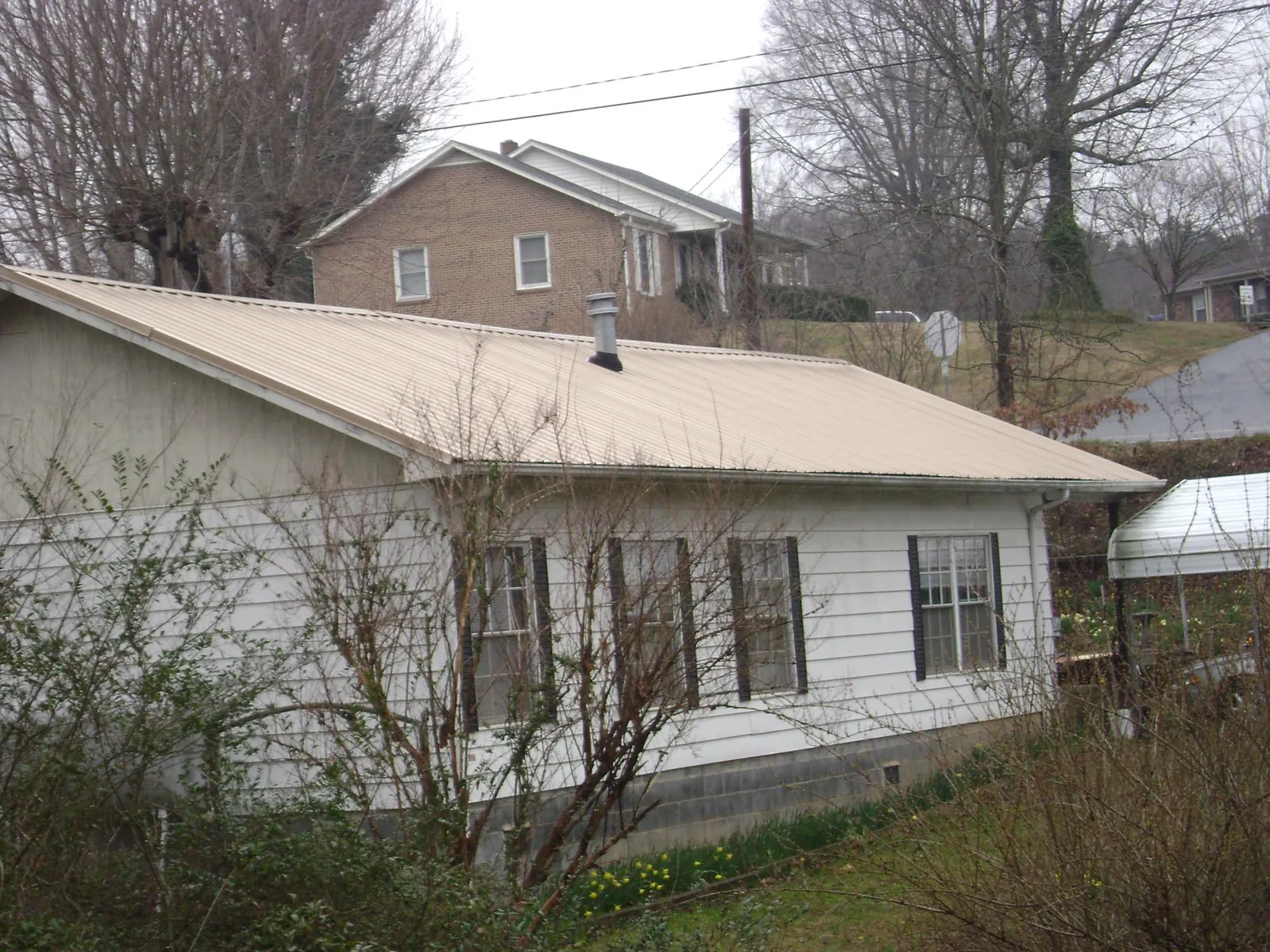 Tan metal roof on a white sided house set into a hillside — Commercial Roofing by Roofing Brothers in Litchfield